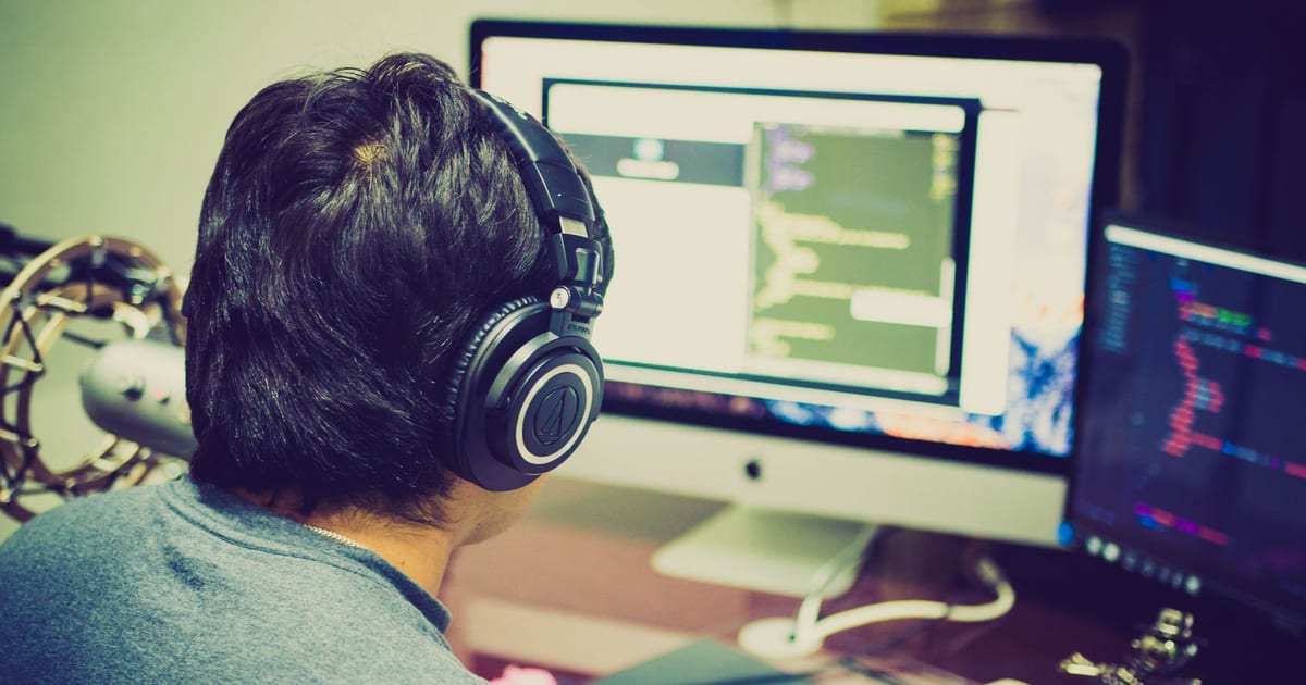 Developer wearing headphones working at a dual-monitor coding setup