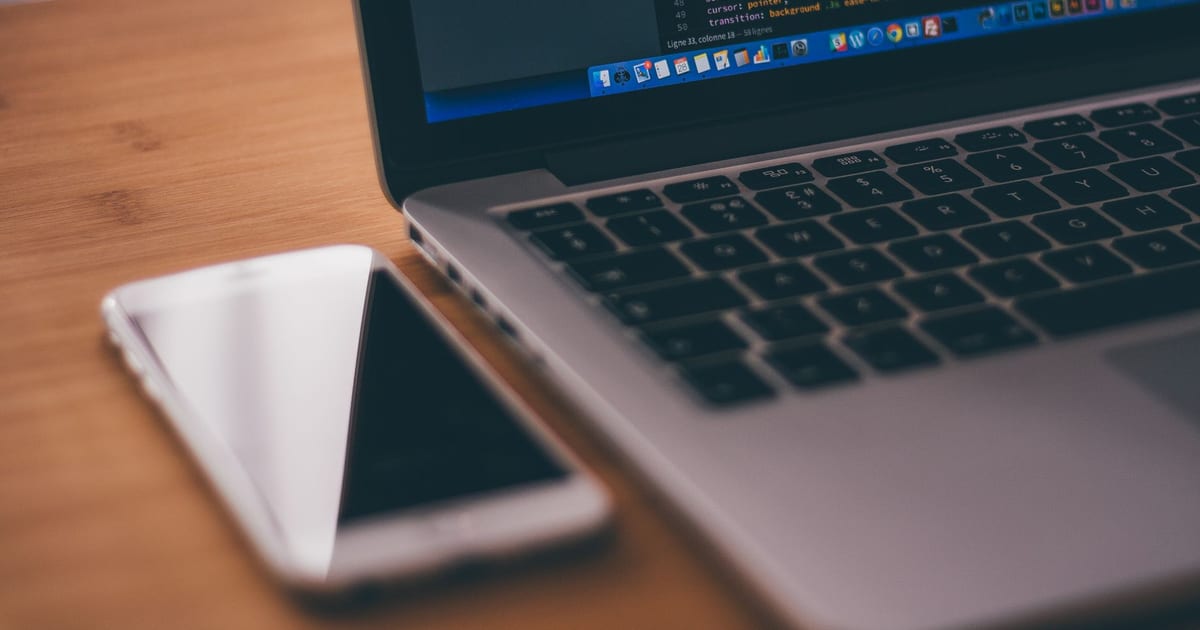 Laptop displaying code beside a smartphone on a wooden desk